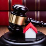Close-up Of House Model With Gavel On Wooden Table In Courtroom
