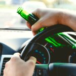 Drunk young man driving a car with a bottle of beer